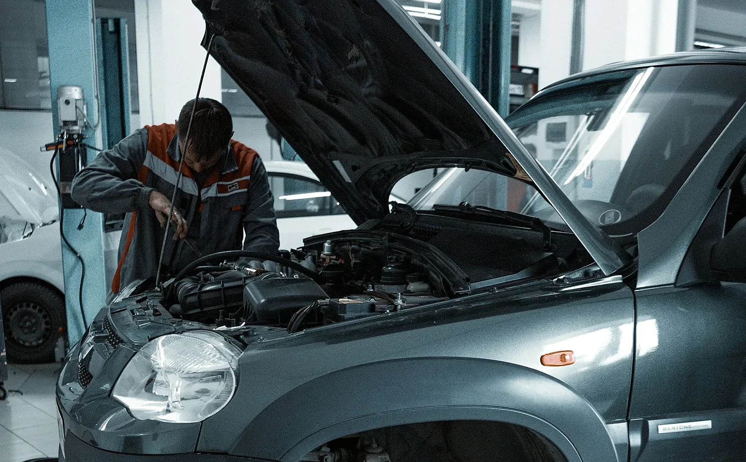 A vehicle on a lift with the hood open while a technician works underneath