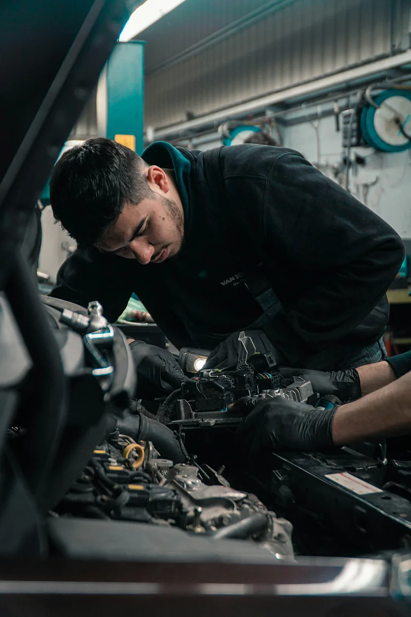 A technician leaning into an engine bay with a work light
