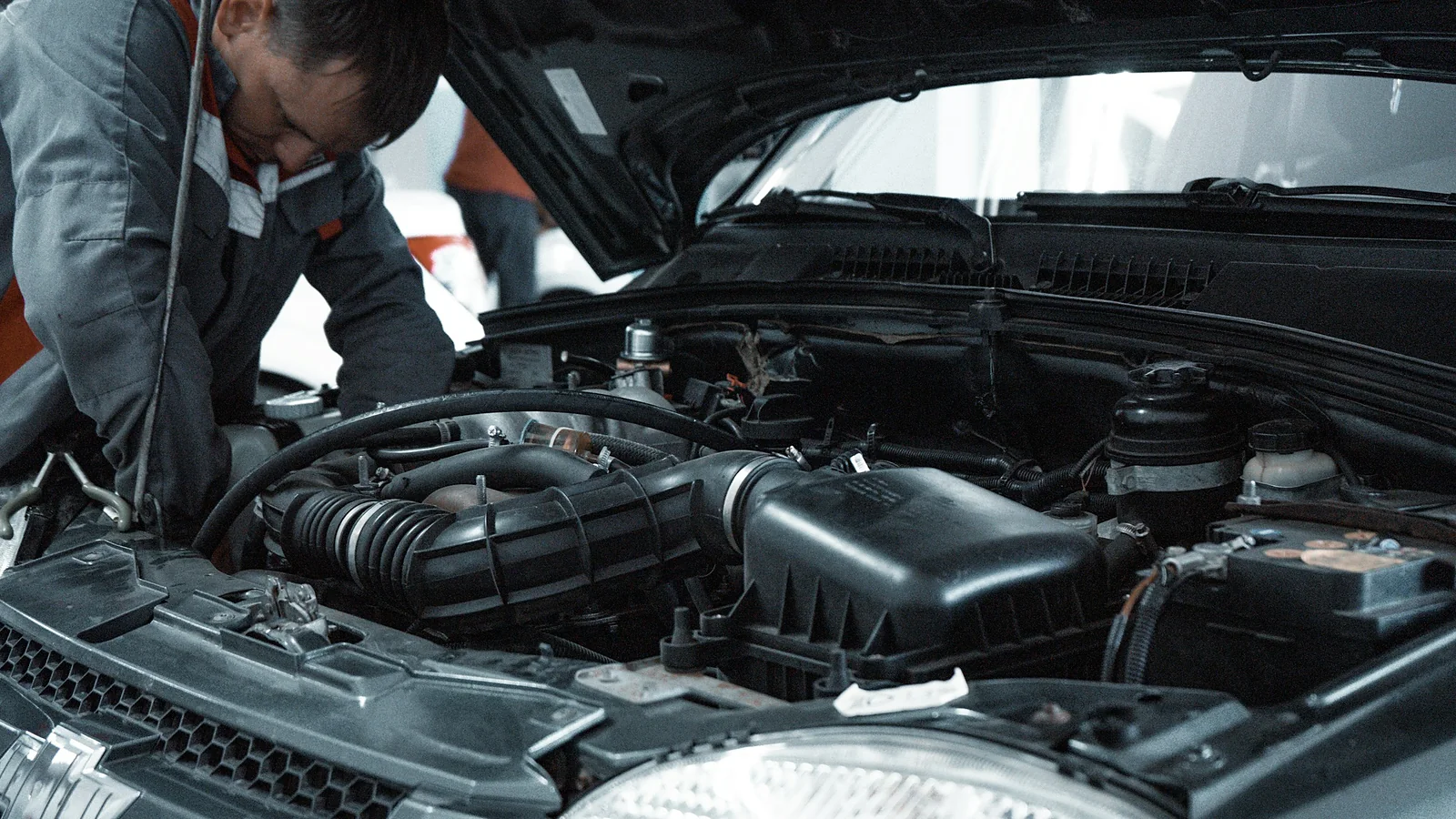 A technician reaching into an open engine bay under shop lighting