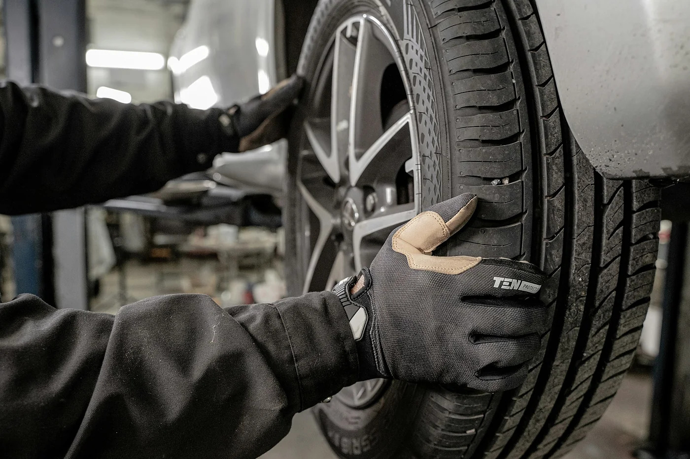 Gloved hands checking tread depth on a tire in a workshop