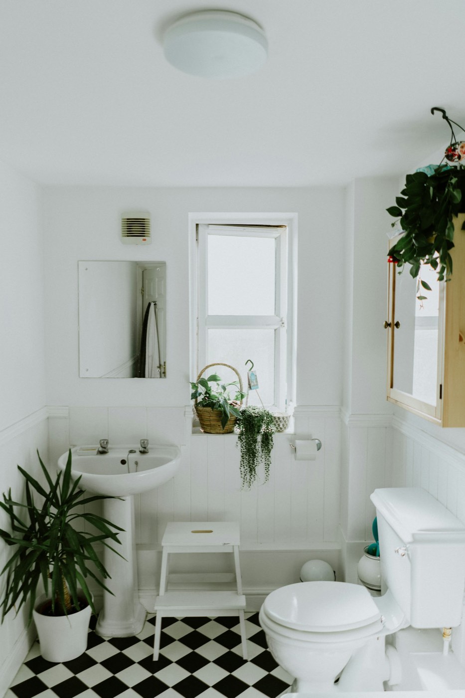 Small white bathroom with a pedestal sink, a toilet, and a black and white checkered floor
