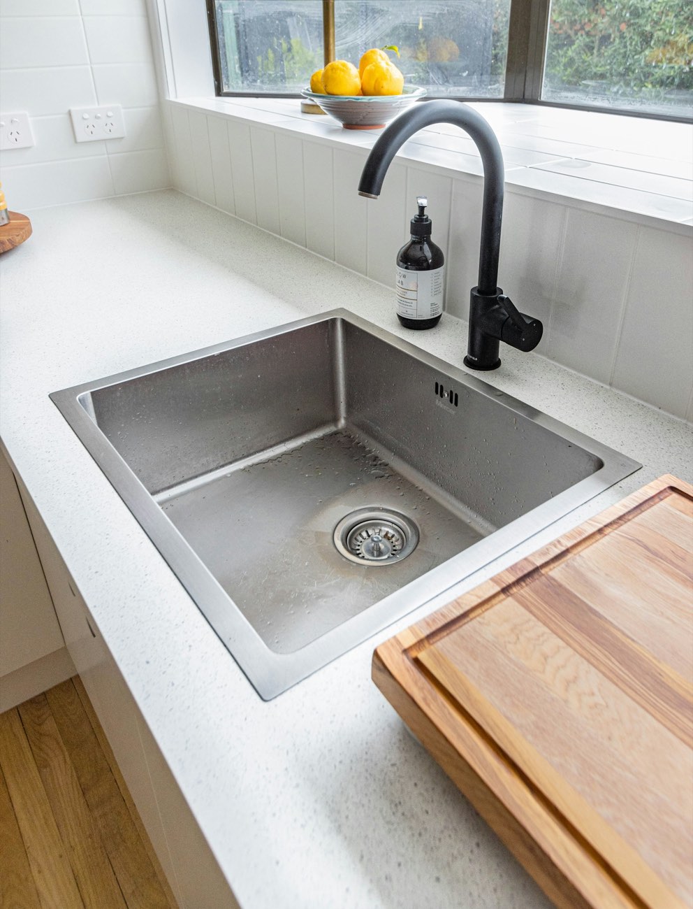 Stainless steel sink in a white stone counter, next to a wooden cutting board