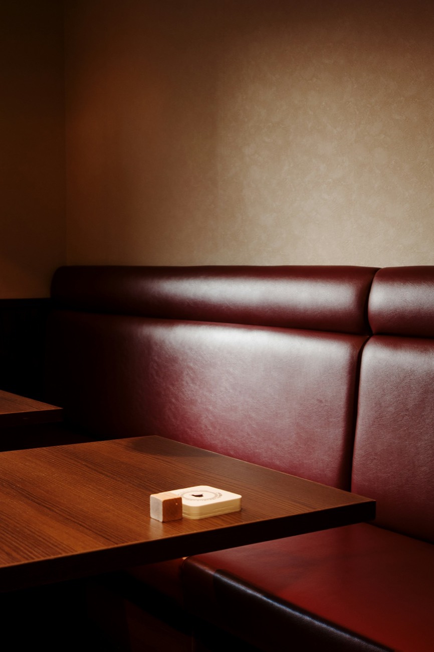 An empty oxblood leather booth beside a wooden table in low light