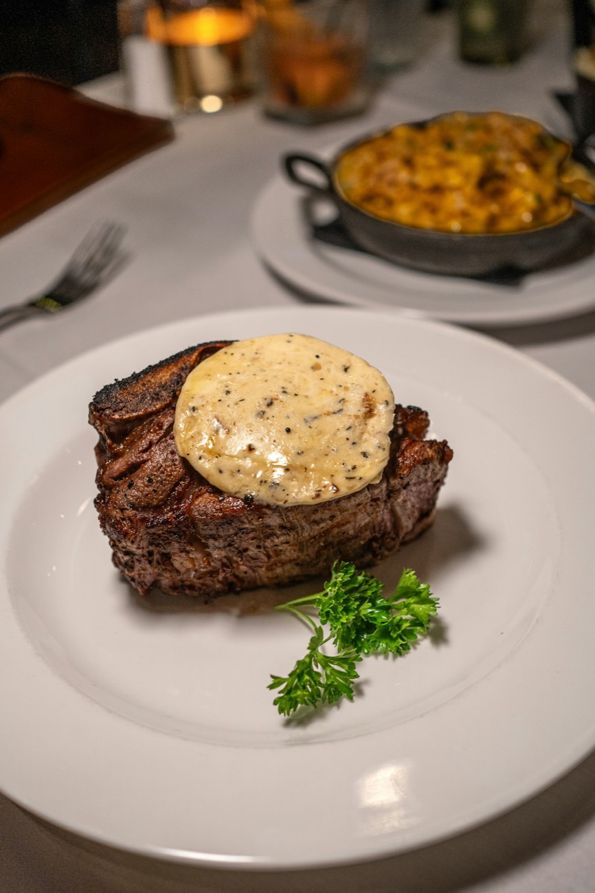 A filet topped with a round of herb butter on a white plate, with mac and cheese behind it