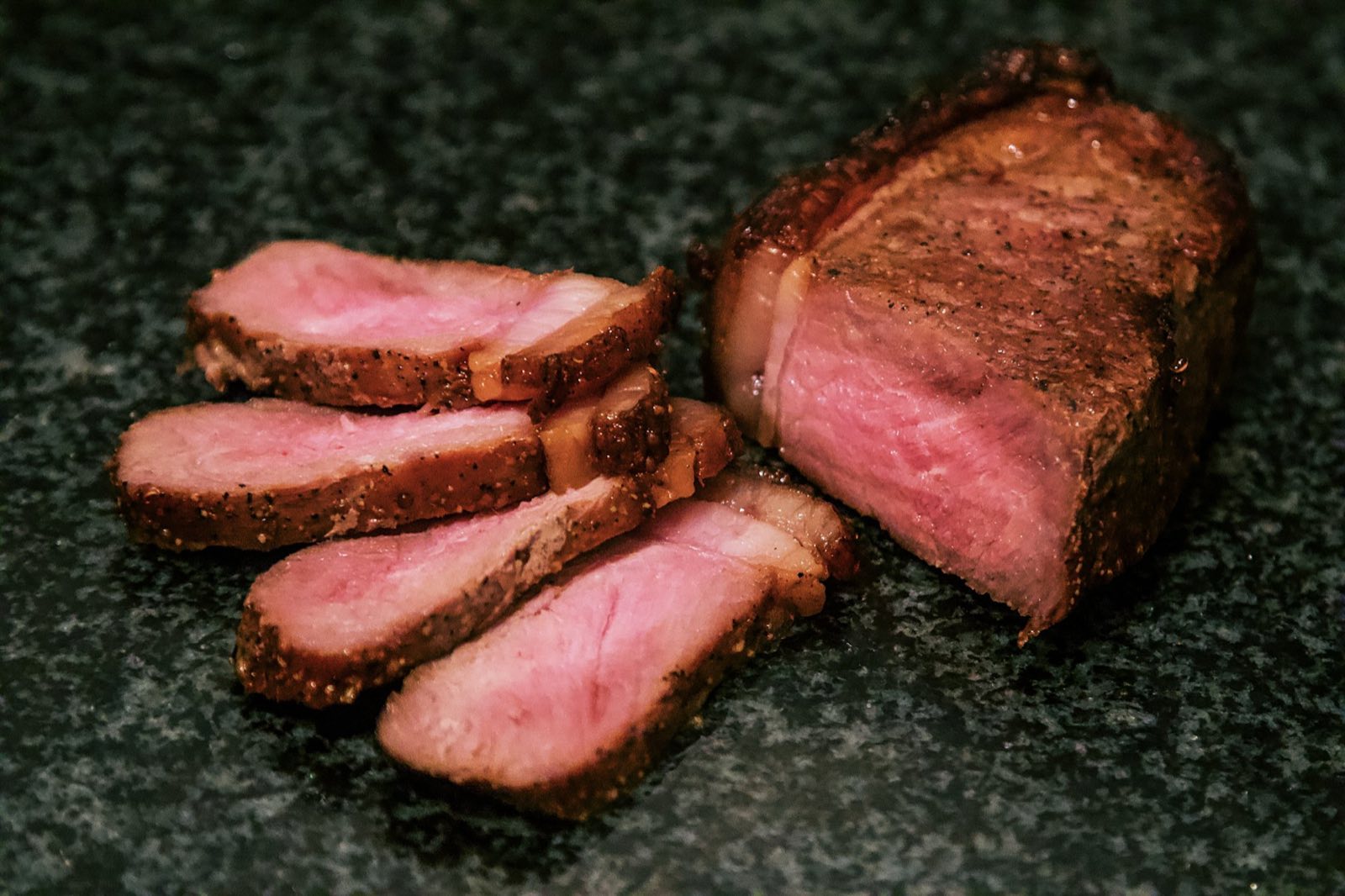 A New York strip cooked medium rare, cut into thick slices on dark stone
